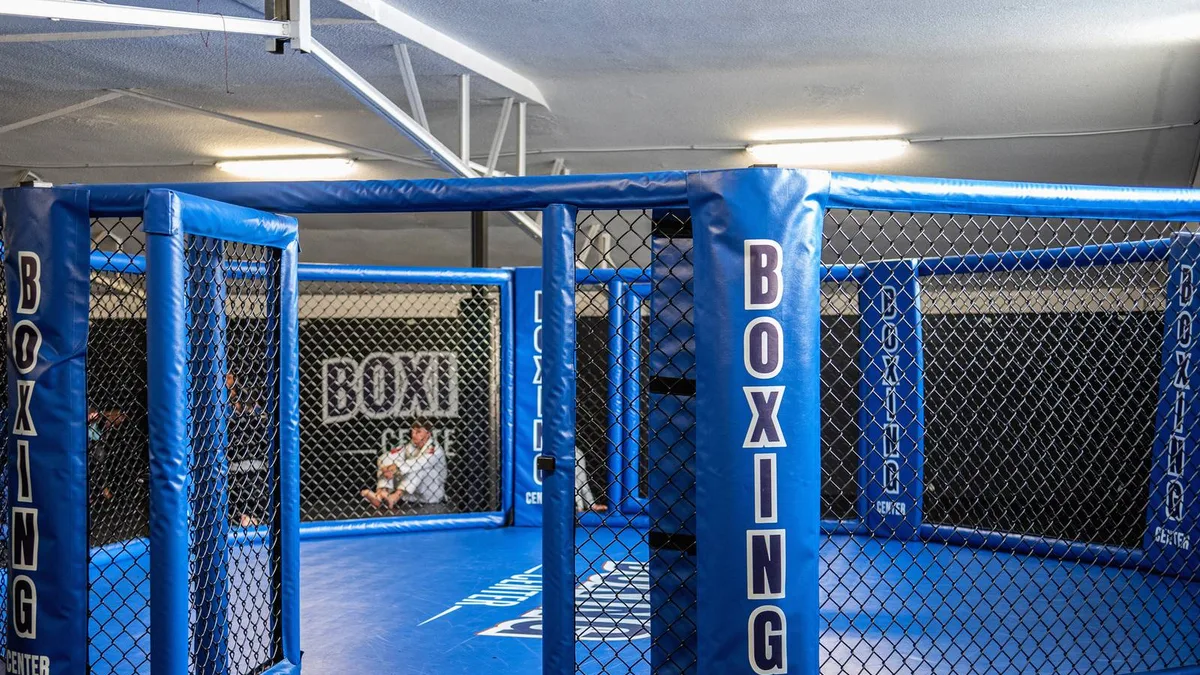 La cage de MMA du Boxing Center Toulouse États-Unis, vide, les poteaux marqués Boxing Center, les tatamis autour.