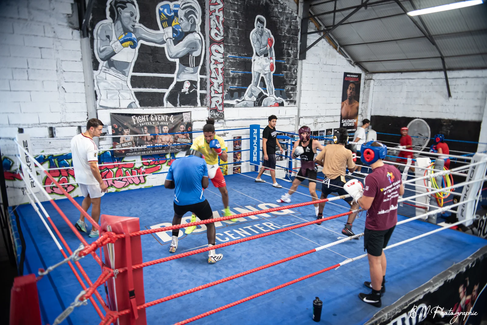 Vue plongeante du ring de compétition Boxing Center avec plusieurs duels de boxe simultanés sous les fresques historiques